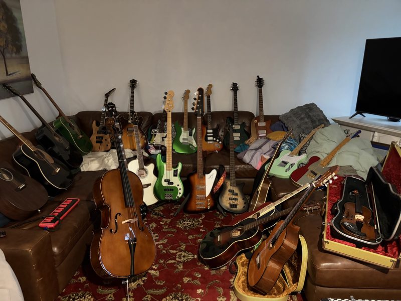 A room packed with electric and acoustic guitars leaning against a leather couch, an upright bass among them.
